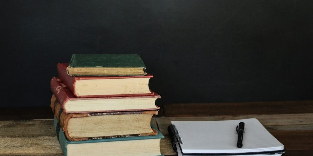 pile of books beside white printer paper and black ballpoint pen